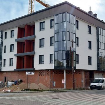 Edificio de apartamentos moderno con paredes blancas, balcones rojos y una fachada de esquina de vidrio en construcción.
