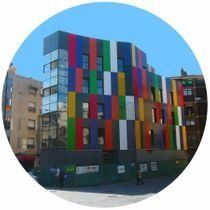 Edificio colorido de varios pisos con paneles verticales de color rojo, azul, verde, amarillo y negro bajo un cielo azul.