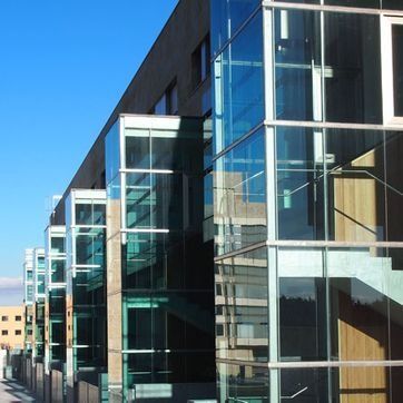 Edificio de oficinas moderno de cristal con ventanas azules reflectantes bajo un cielo despejado.