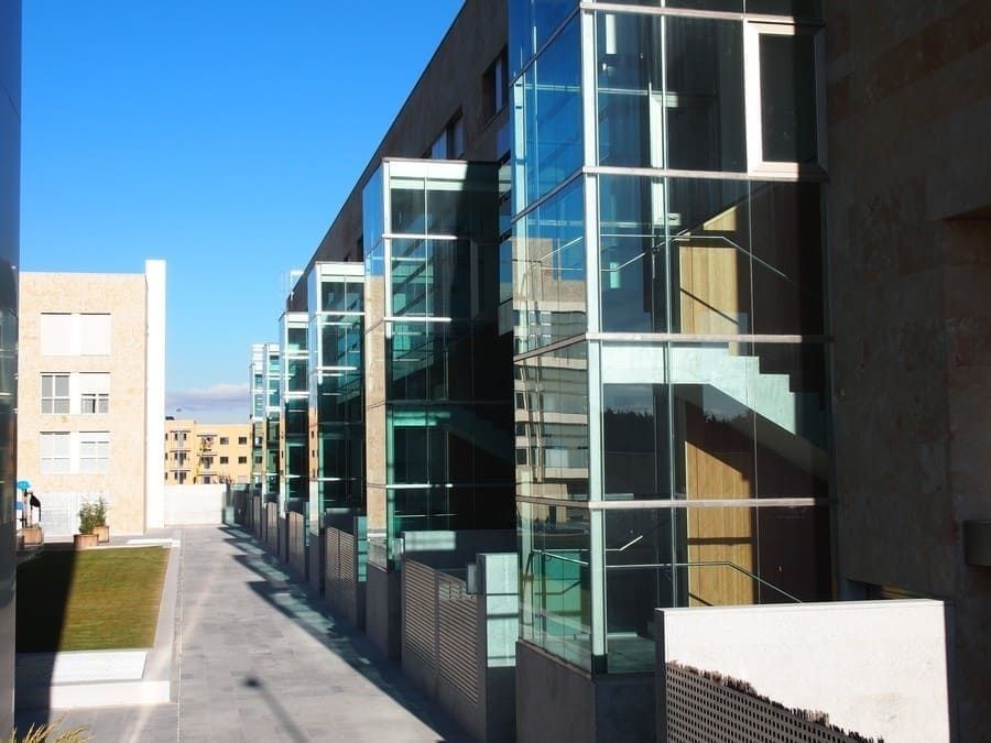 Un moderno pasillo de cristal junto a un paseo pavimentado bajo un cielo azul despejado.