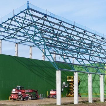 Edificio con estructura de acero en construcción junto a un muro vegetal, con maquinaria de construcción debajo.