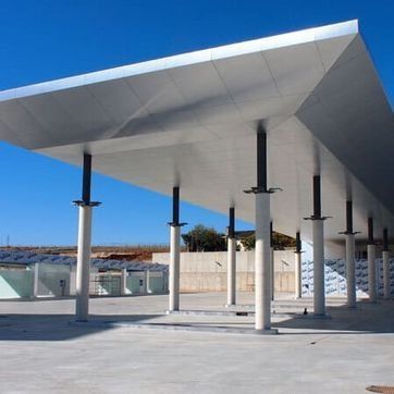 Pabellón moderno al aire libre con una gran marquesina blanca sostenida por columnas blancas y negras bajo un cielo azul.