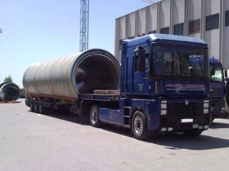 Un camión azul transporta una tubería grande en un remolque.