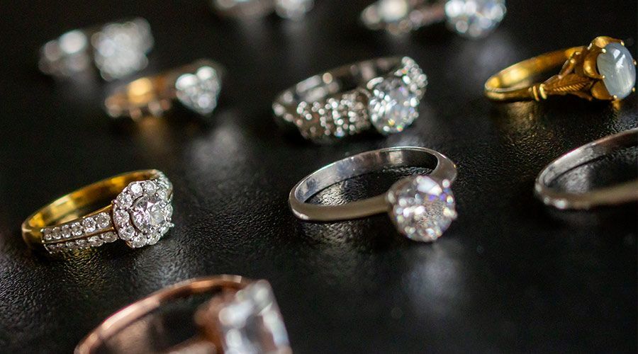 Anillos de diamantes y oro expuestos sobre una superficie oscura, con varios de ellos borrosos al fondo.