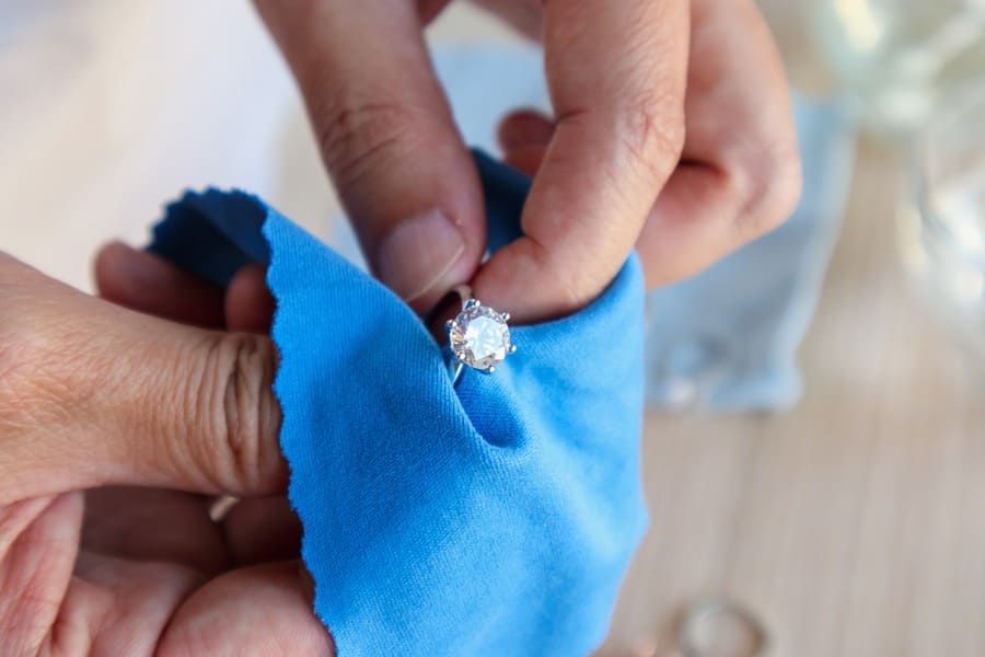 Manos colocando un anillo de diamantes sobre una tela azul en una toma de primer plano.