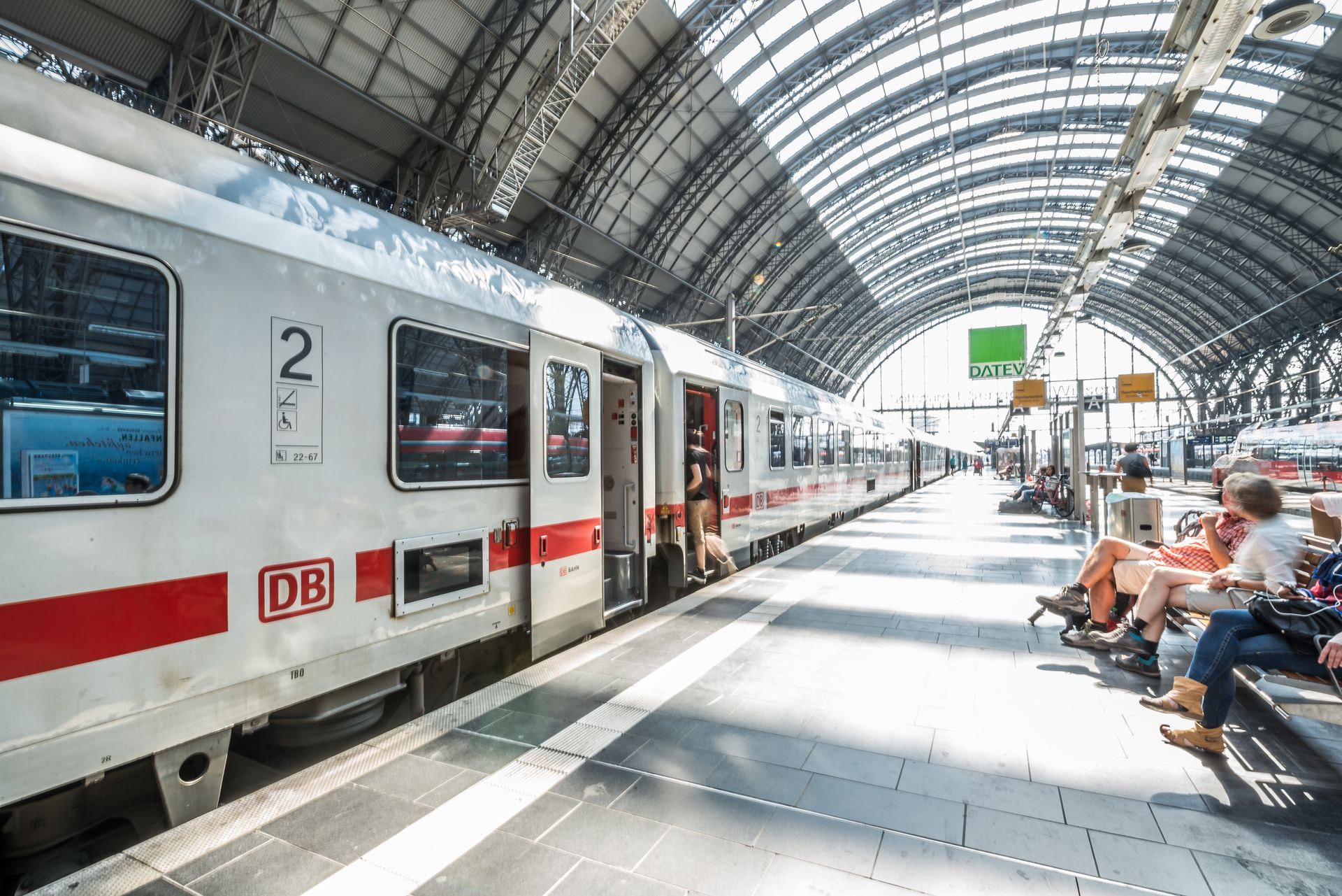 Train moderne sur un quai de gare lumineux et voûté, avec des passagers assis et le logo de la DB