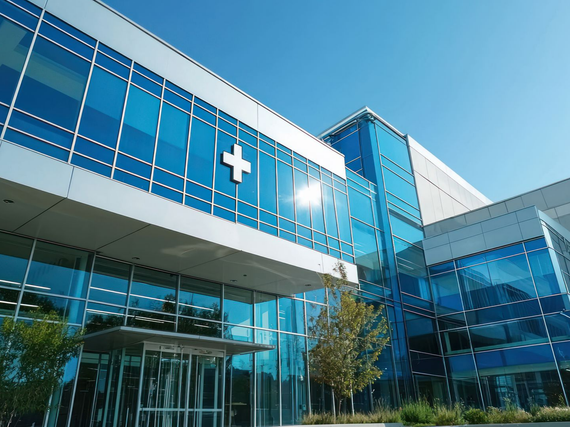 Bâtiment hospitalier moderne en verre avec des fenêtres bleues et une croix médicale blanche