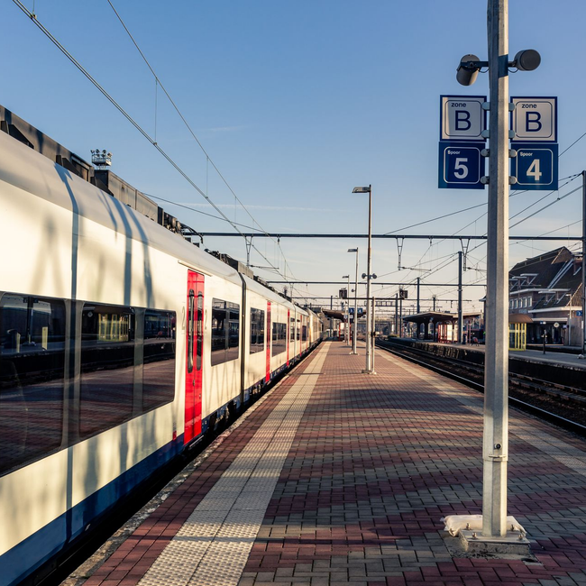 Quai de gare vide avec un train blanc stationné et des panneaux de signalisation bleus sous un ciel dégagé