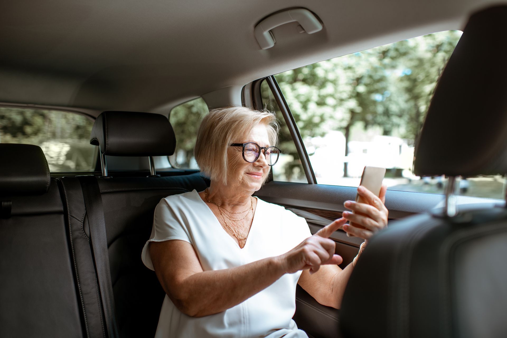 Une femme assise sur un siège auto, souriante tout en utilisant un smartphone.
