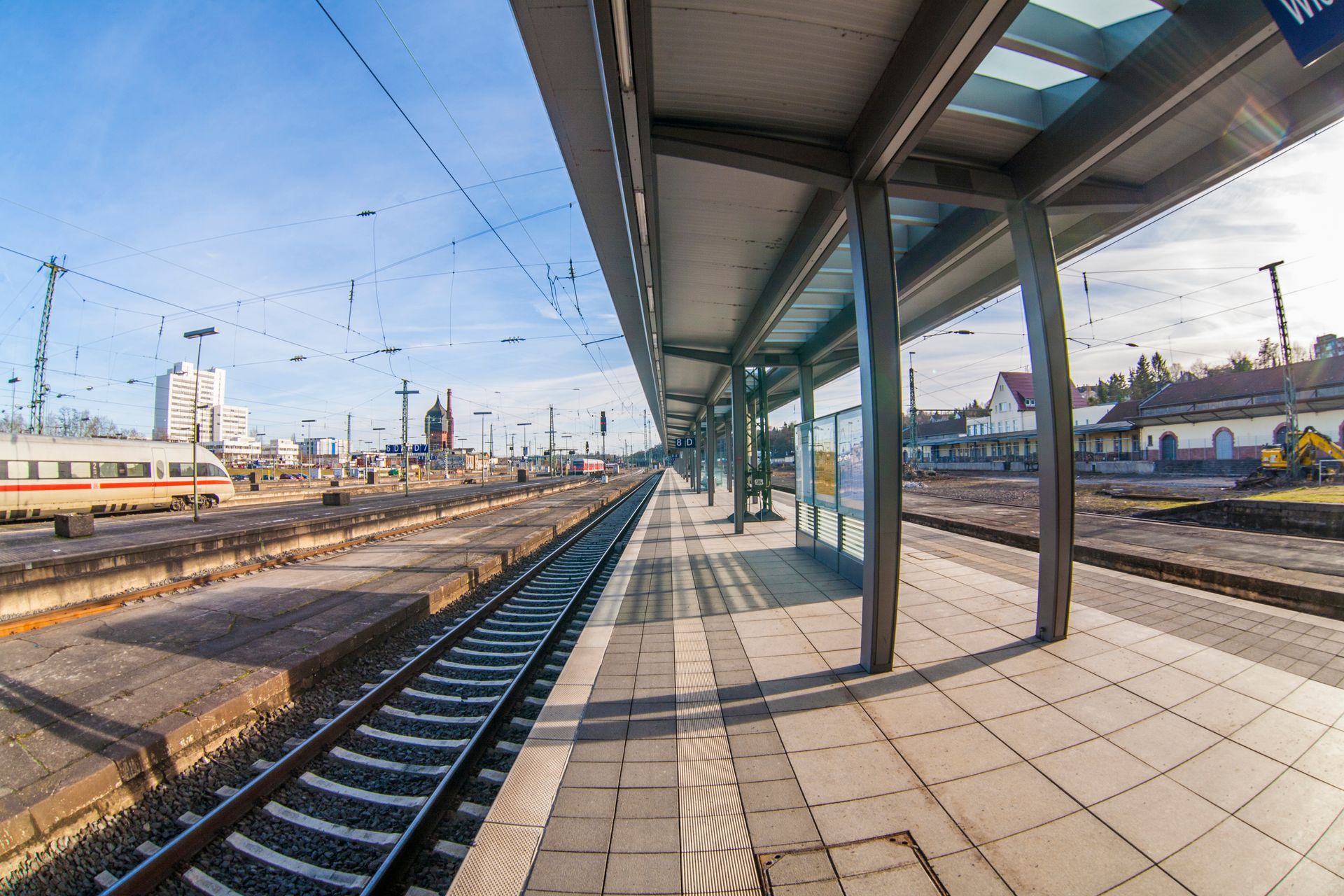 Quai de gare désert, le long des voies, sous un ciel bleu azur.