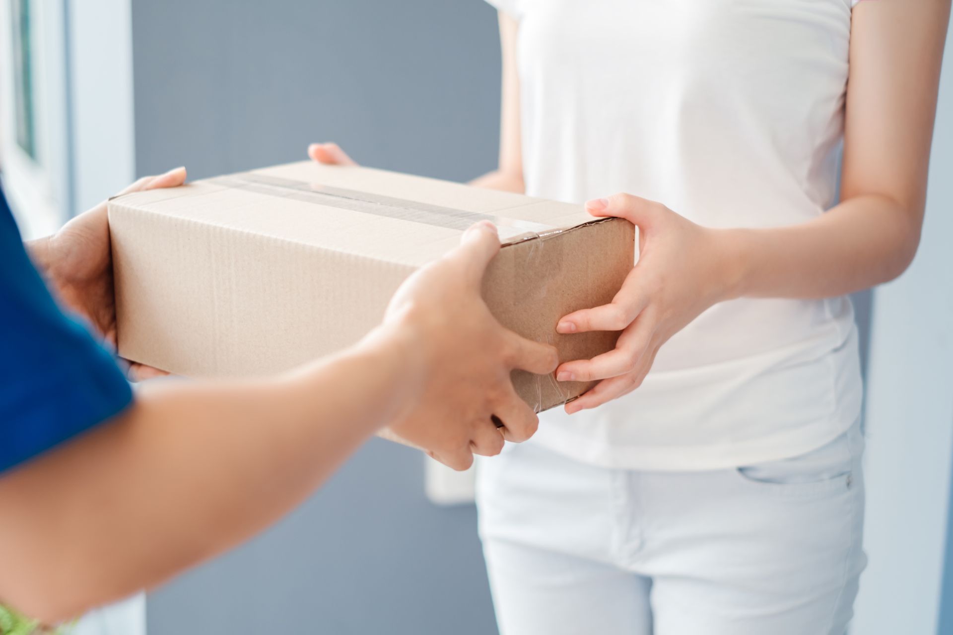 Des mains se passent une boîte en carton dans une pièce lumineuse