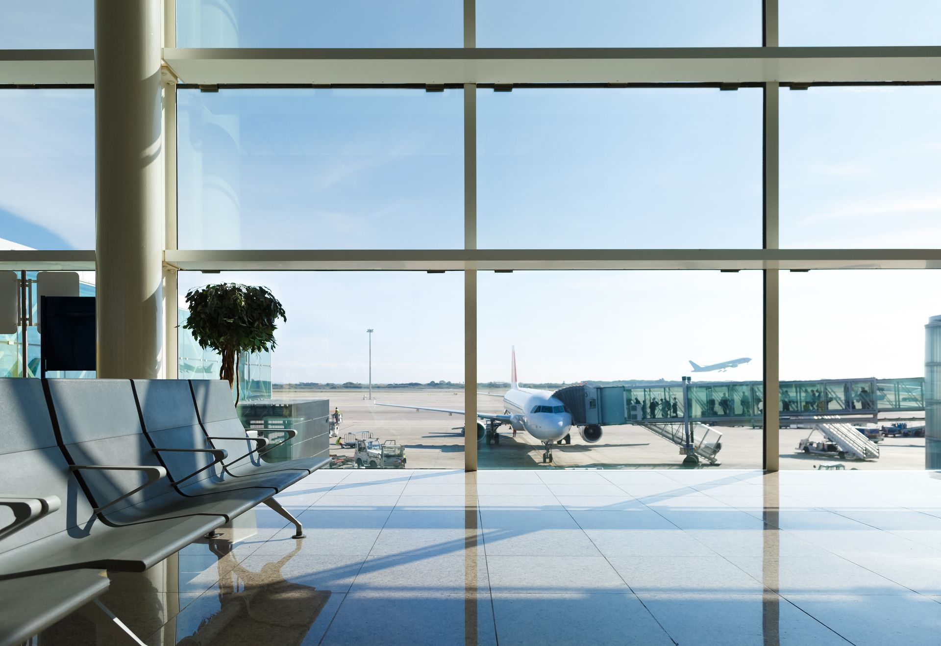 Salon d'aéroport vide avec de grandes fenêtres donnant sur la piste et les avions stationnés.