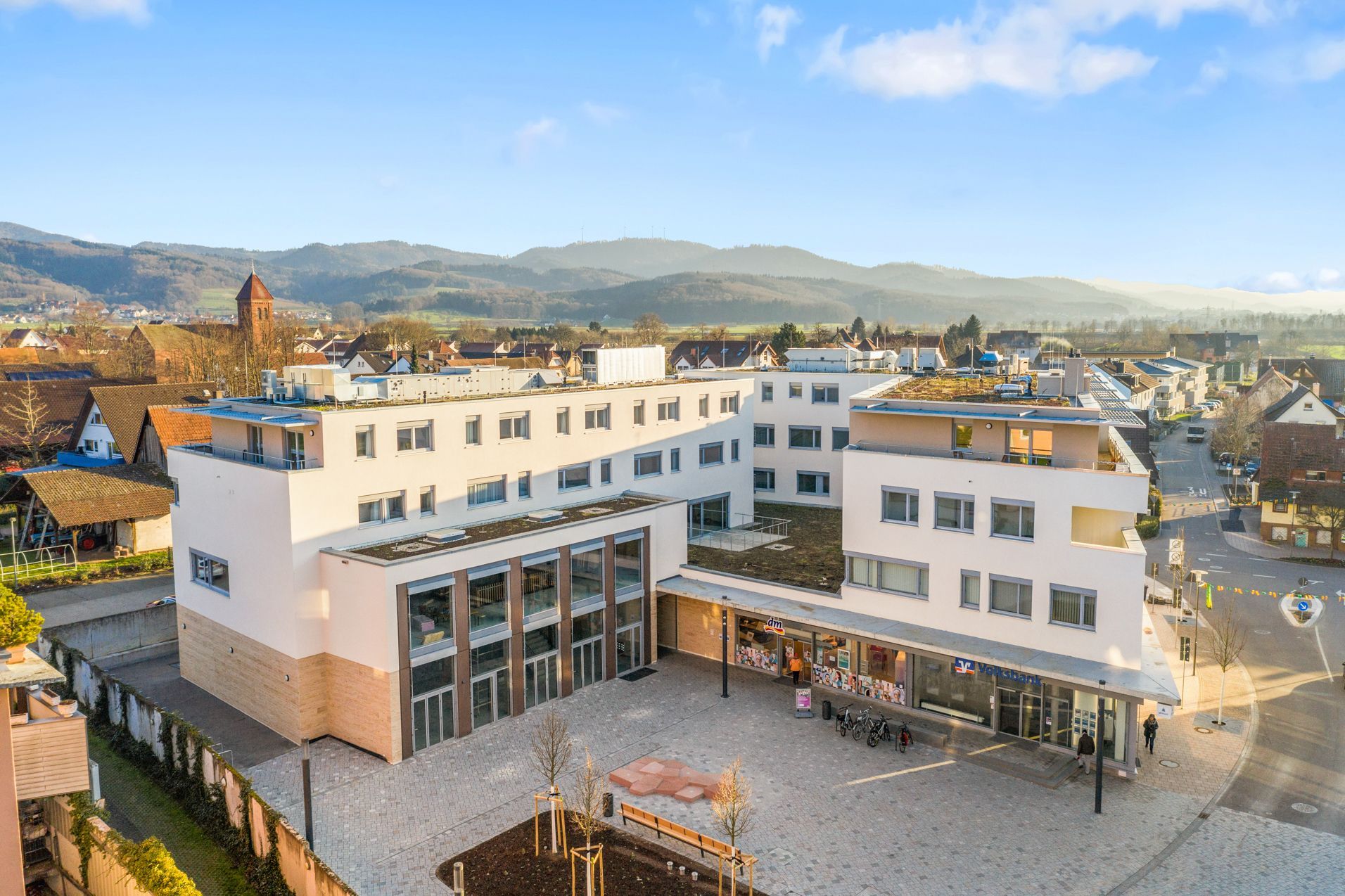 Eine Luftaufnahme eines großen weißen Aparthotel in Denzlingen mit Bergen im Hintergrund.