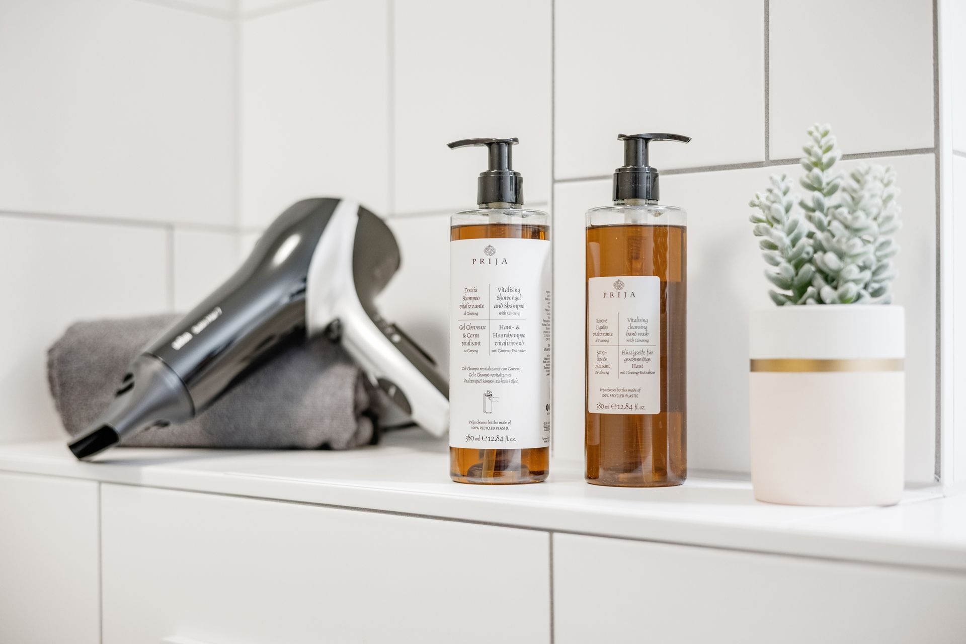 Zwei Flaschen Shampoo und Spülung stehen auf einer Badezimmerablage neben einem Haartrockner.