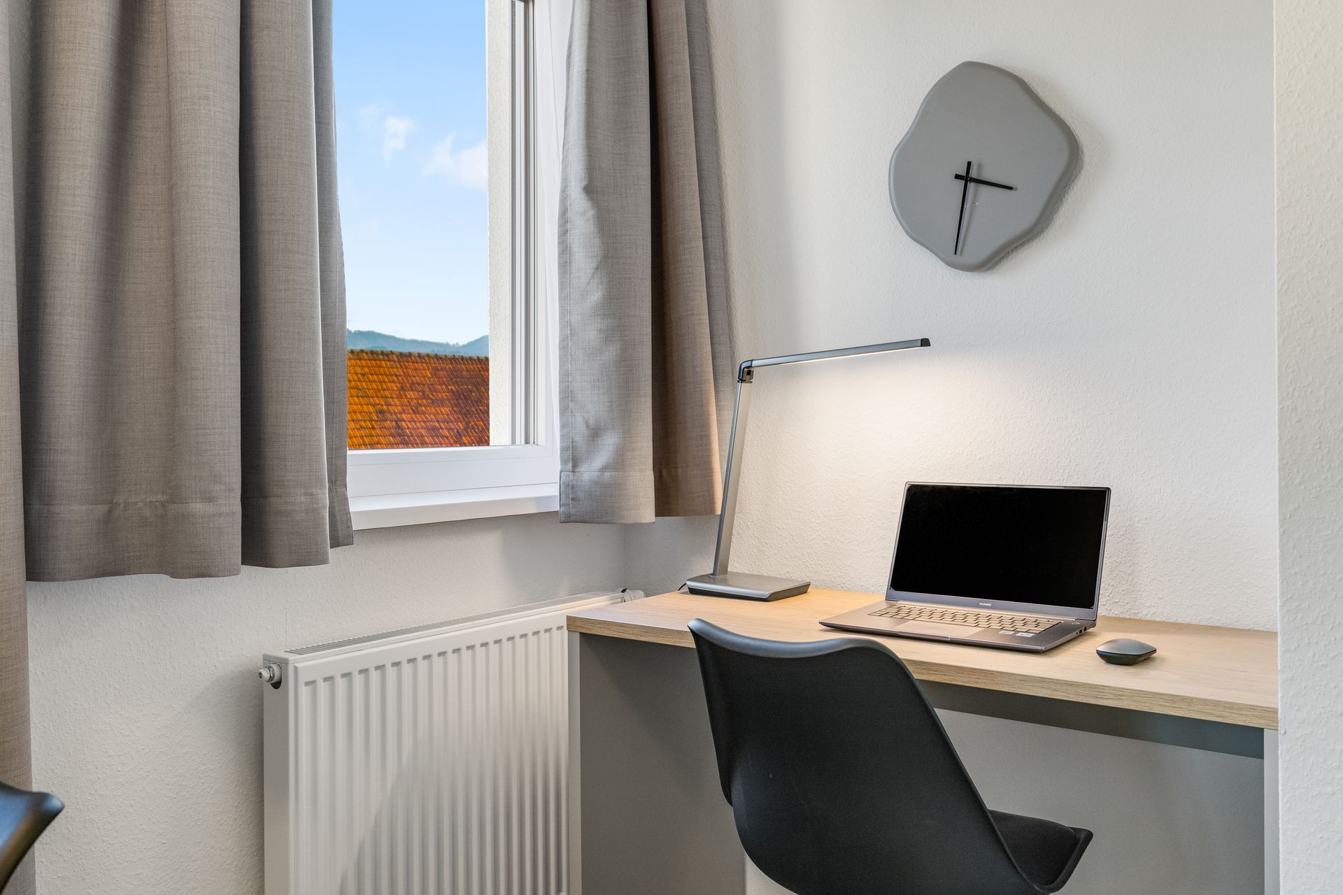 Ein Schreibtisch mit einem Laptop darauf und einer Uhr an der Wand.