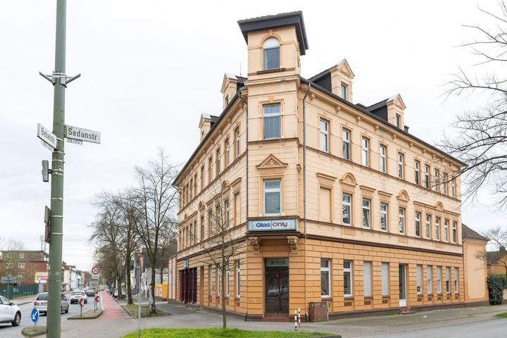 An einer Straßenecke steht ein großes Gebäude mit vielen Fenstern.