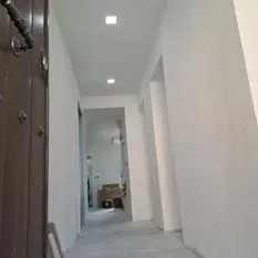 Un largo pasillo con paredes blancas y una puerta marrón que conduce a una sala de estar.