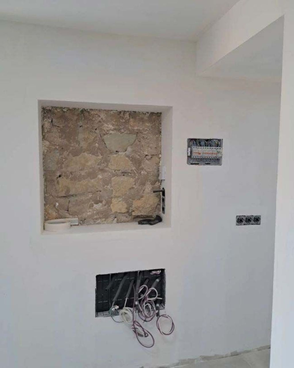 Una pared blanca con un agujero y una pared de piedra detrás.