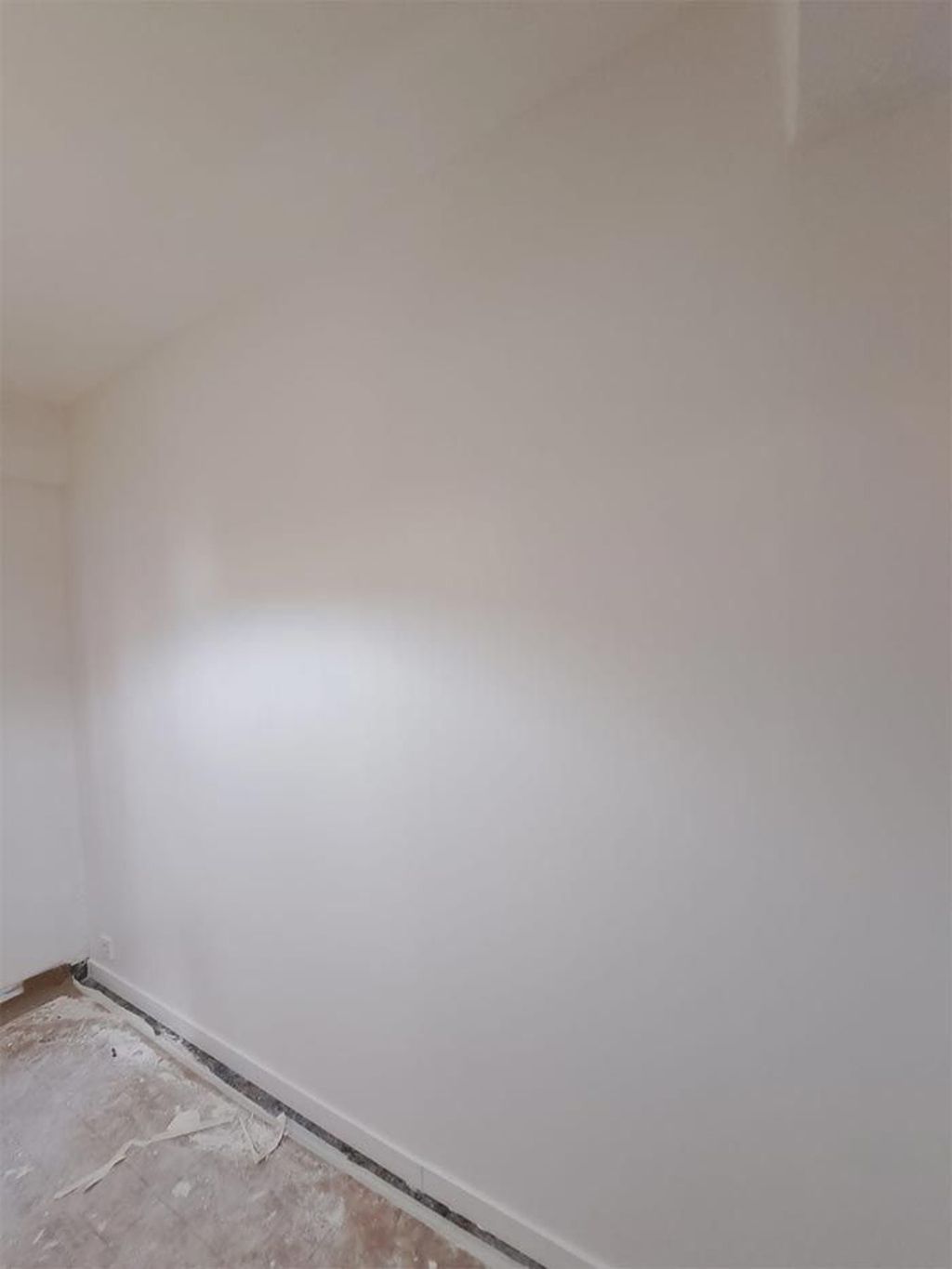 Una habitación con una pared blanca y un suelo de madera.