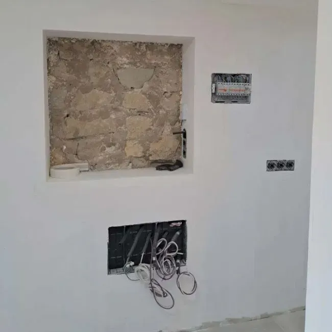Una pared blanca con un agujero y una pared de piedra detrás.