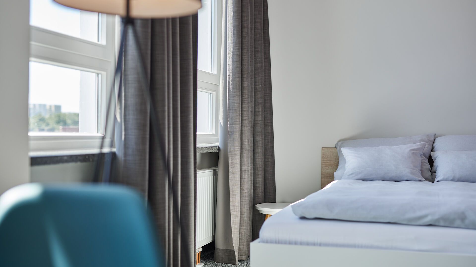 Ein Schlafzimmer mit Bett, Stuhl, Lampe und Fenster.