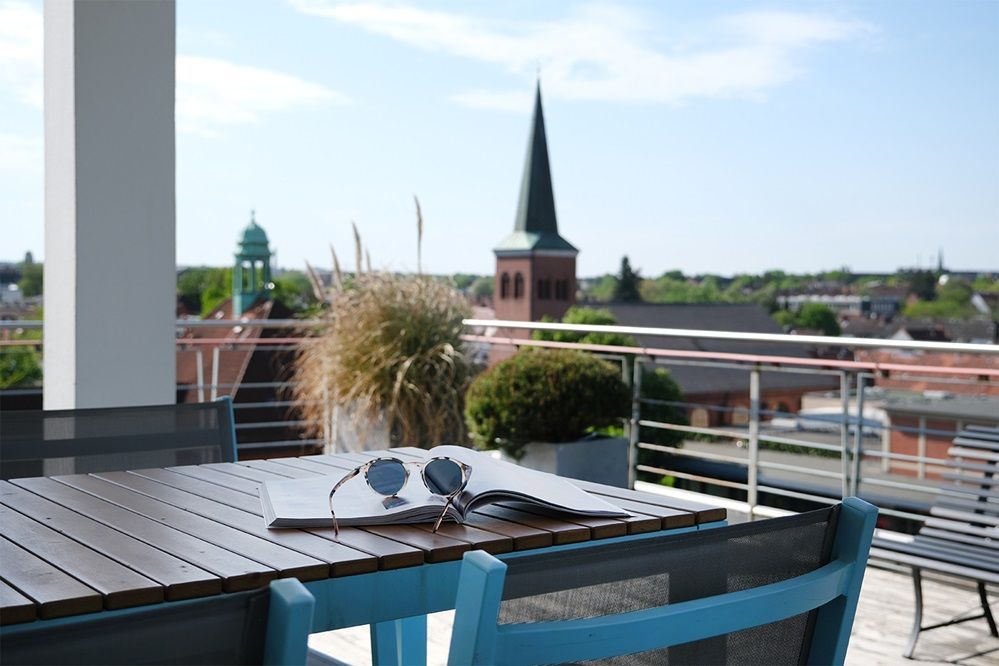 Ein Tisch mit einem Laptop und einer Sonnenbrille darauf und im Hintergrund ein Blick auf eine Kirche.