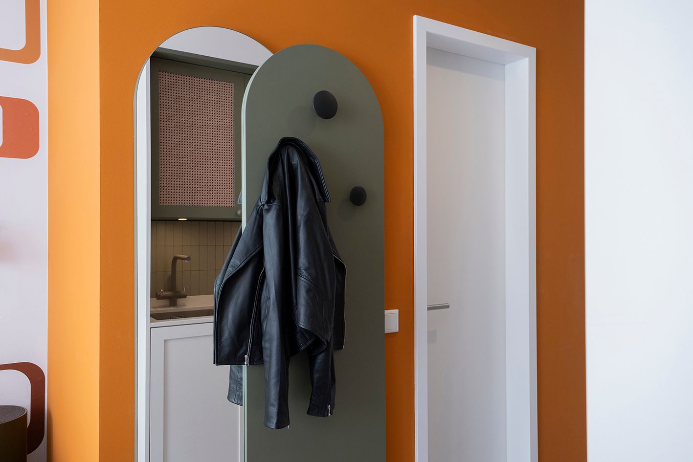 Eine Garderobe mit einer daran hängenden Jacke in einem Flur neben einer Tür.