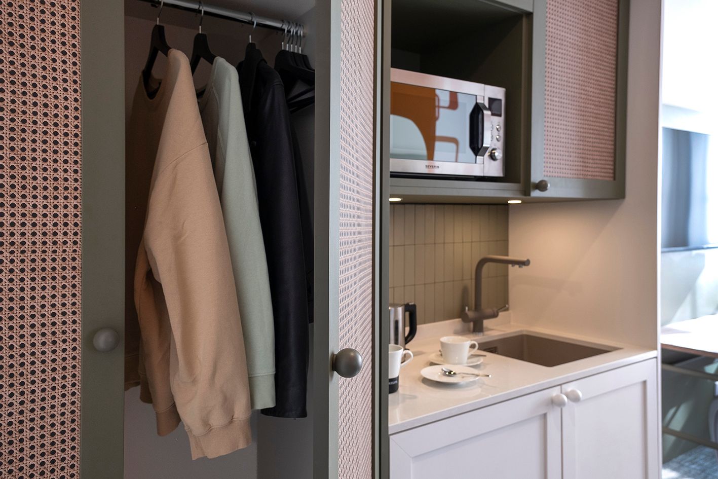 Eine Küche mit Mikrowelle, Spüle und in einem Schrank hängender Kleidung.