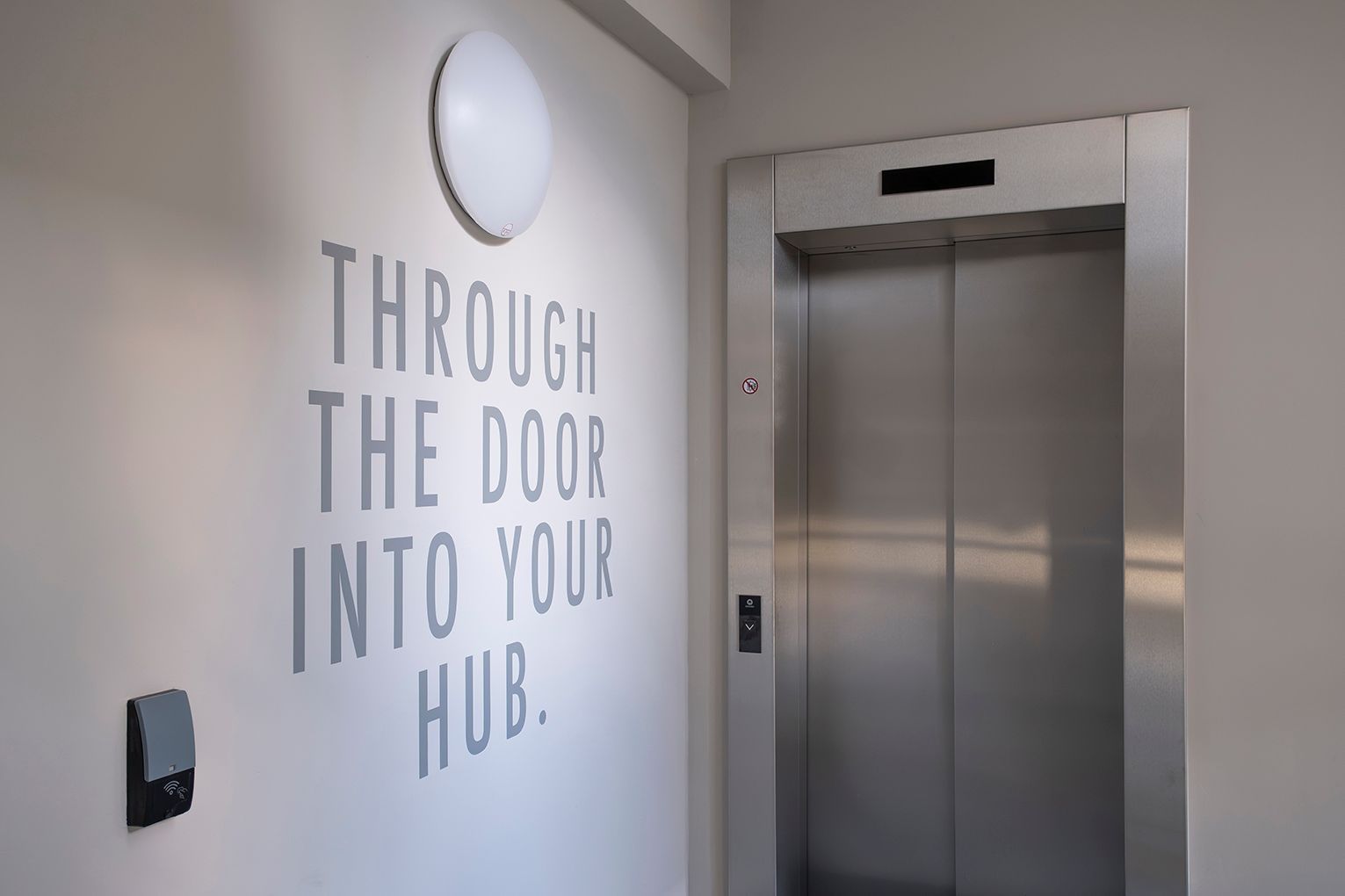 Fahrstuhl im HUB Apartments – daneben ein Schriftzug "Through the door into your HUB"