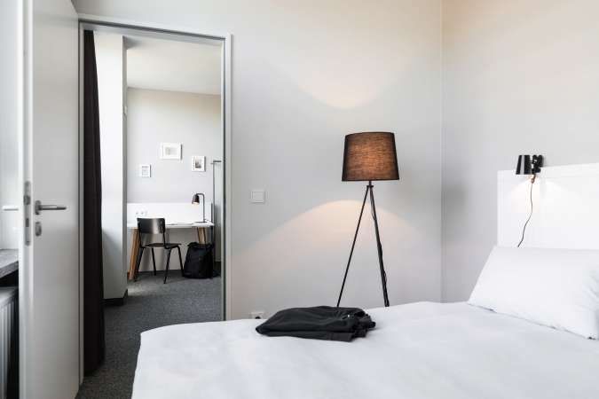 Ein Schlafzimmer mit Bett, Lampe, Schreibtisch und Stühlen.