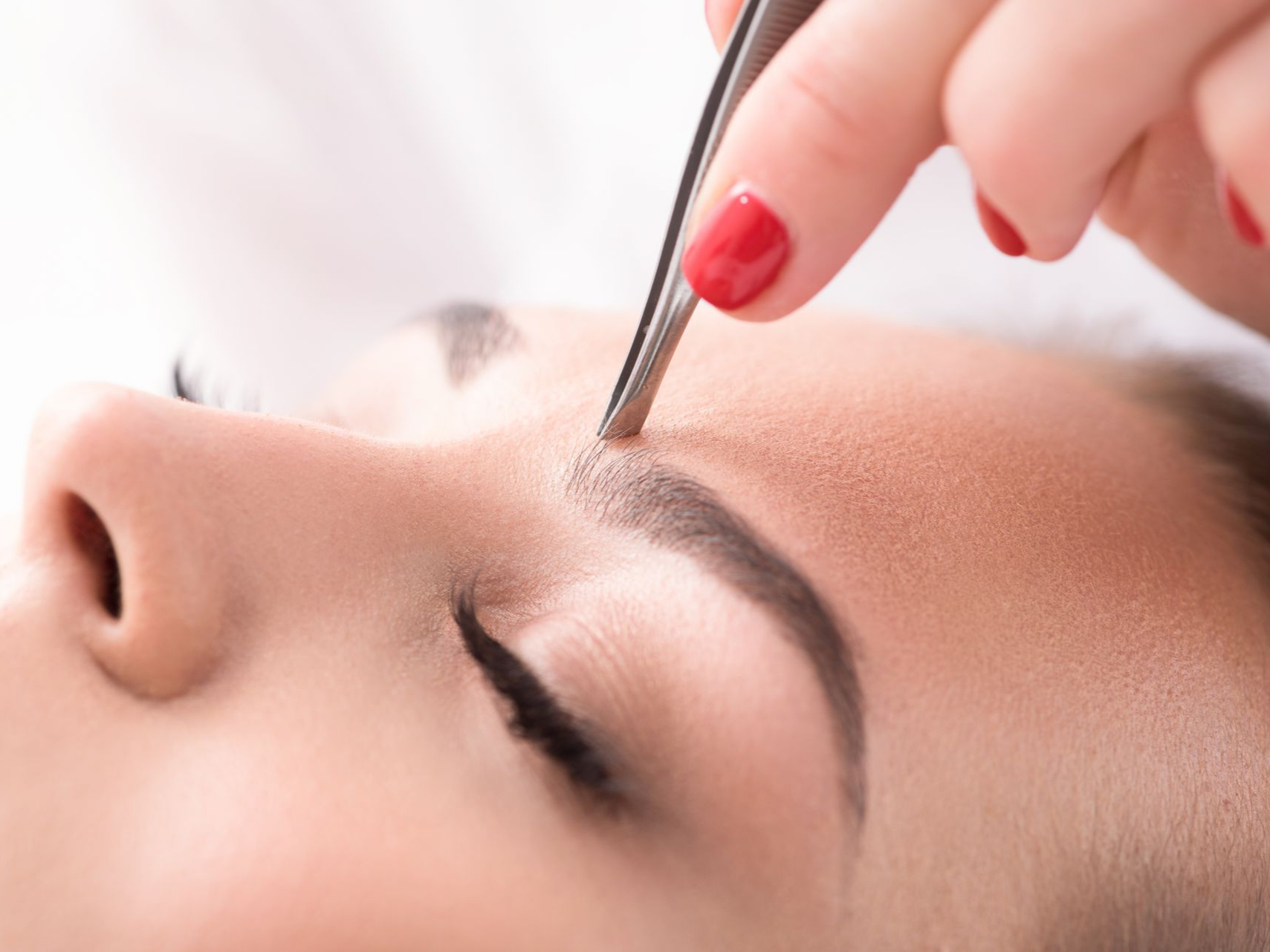 Personne se faisant épiler la lèvre supérieure à la cire ; esthéticienne appliquant la cire avec une spatule en bois.