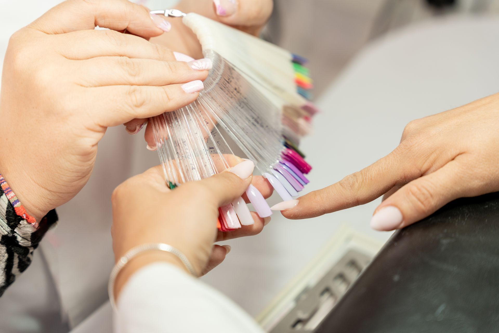 Une personne choisit une couleur de vernis à ongles parmi celles présentées par une autre personne dans un salon de manucure.