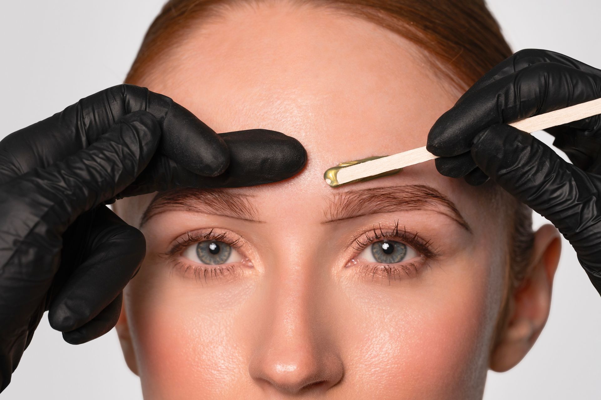 Les sourcils d’une personne sont épilés à la cire par une personne portant des gants noirs.