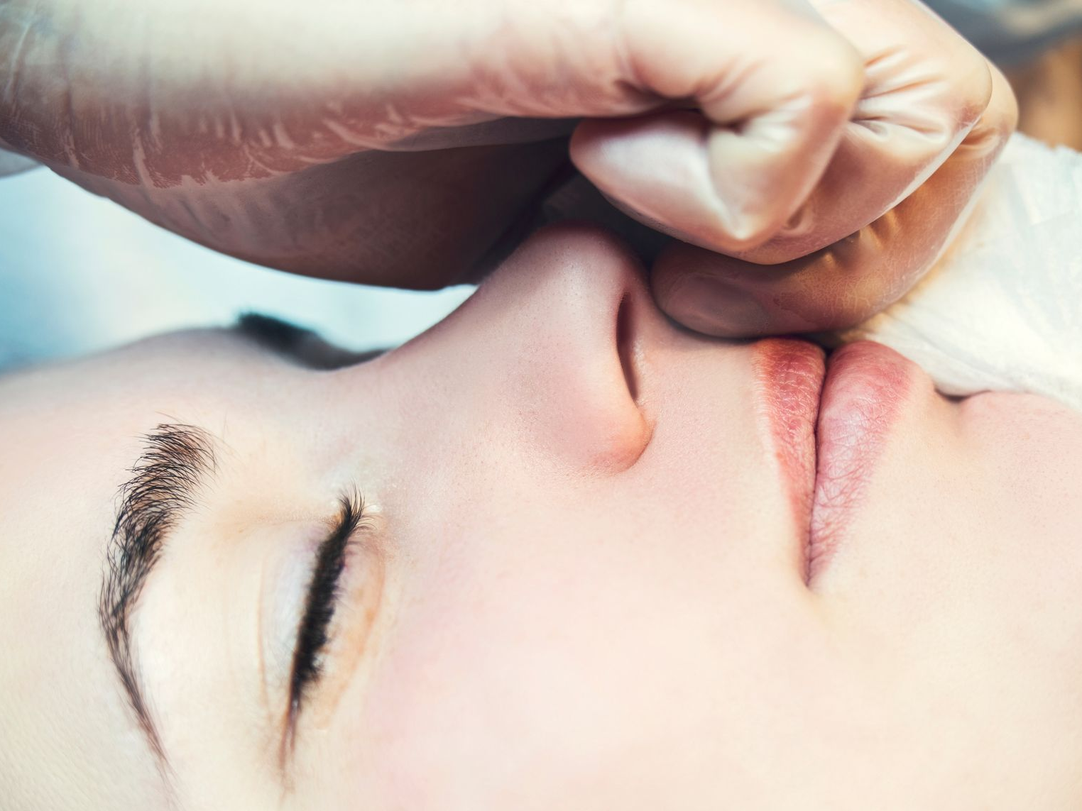 Gros plan sur le visage d'une personne aux yeux fermés, une main gantée touchant son nez.