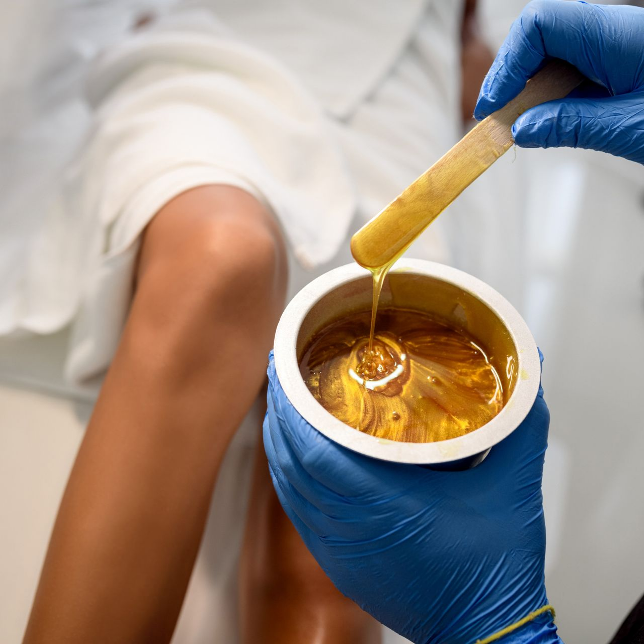 Personne se faisant épiler les jambes à la cire dorée par une main gantée.