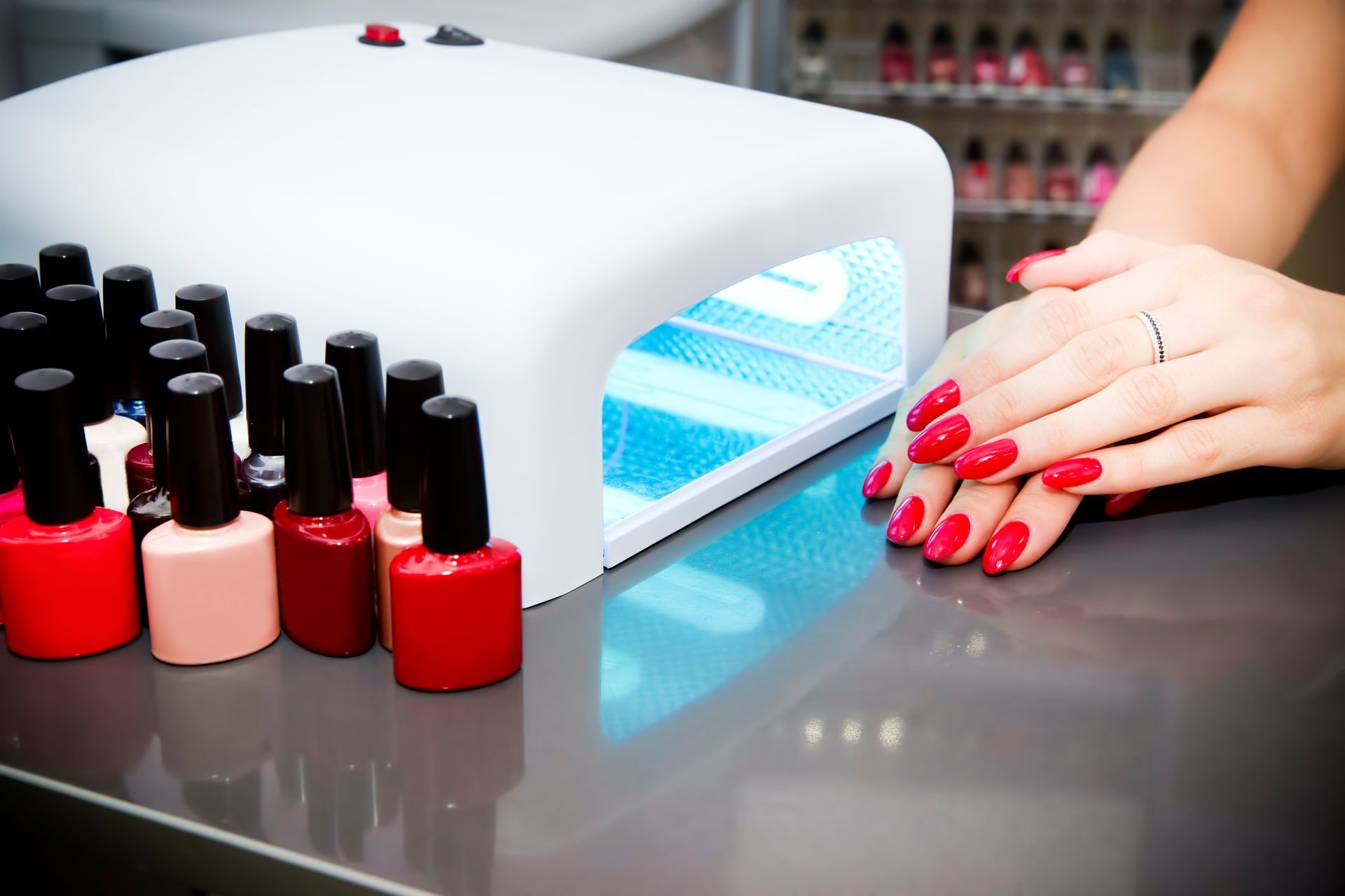 Mains de femme avec du vernis à ongles rouge à côté de flacons de vernis et d'une lampe UV.