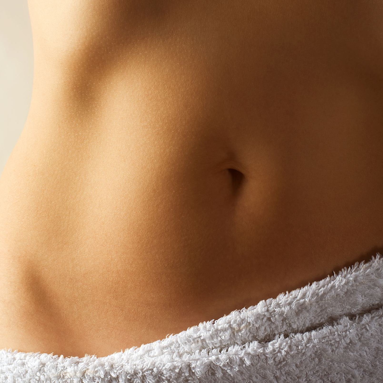 Gros plan sur le torse d'une personne, peau bronzée, nombril visible, partiellement enveloppée dans une serviette blanche.
