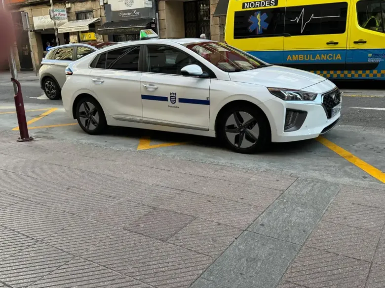 Un sedán blanco con el logotipo en la puerta estaba detenido en una calle junto a una ambulancia y un bordillo 