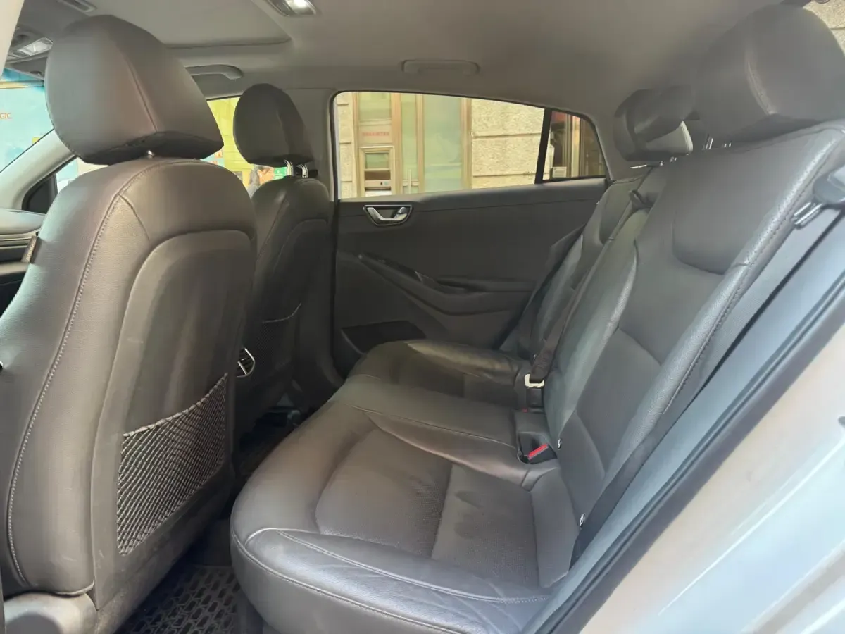 Asiento trasero vacío de un coche beige con asientos y reposacabezas de cuero gris, visto desde la puerta trasera abierta.