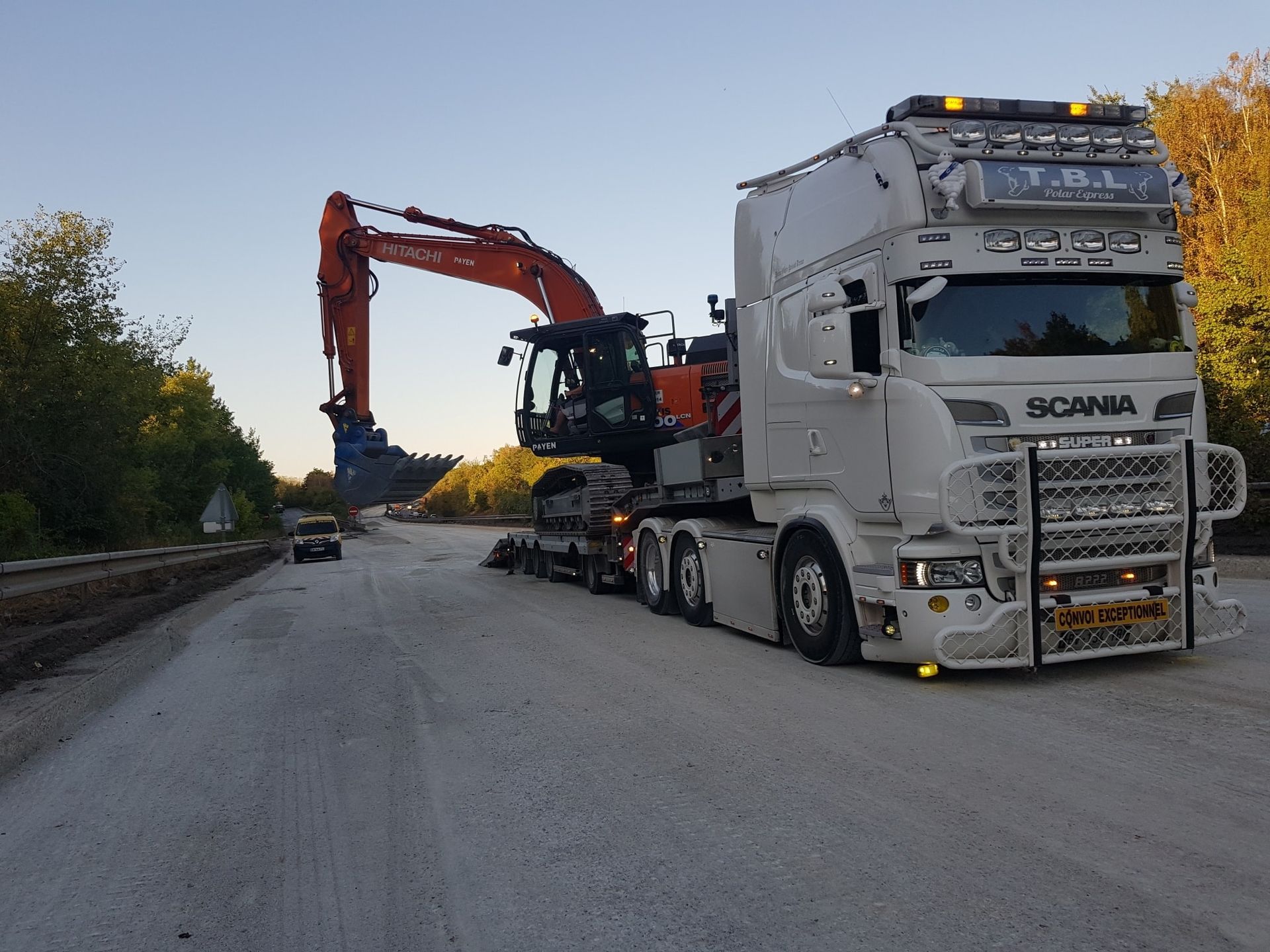 Une pelleteuse rouge sur un porte-engins sur une autoroute en travaux