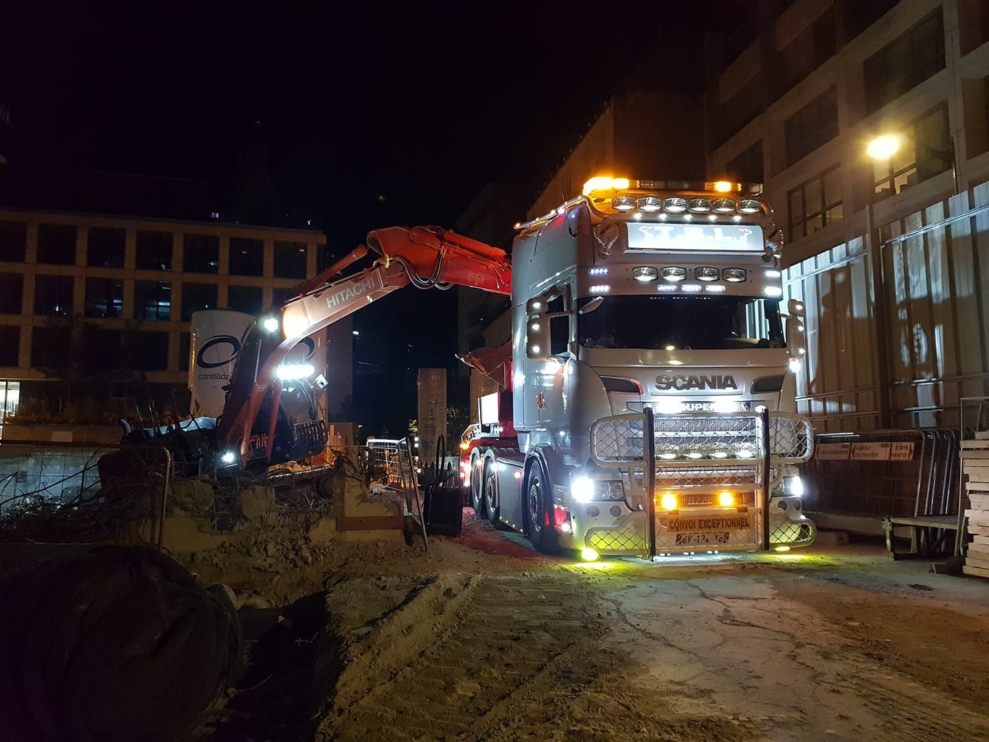 Pelleteuse rouge sur un chantier de nuit à côté du poids lourd Scania