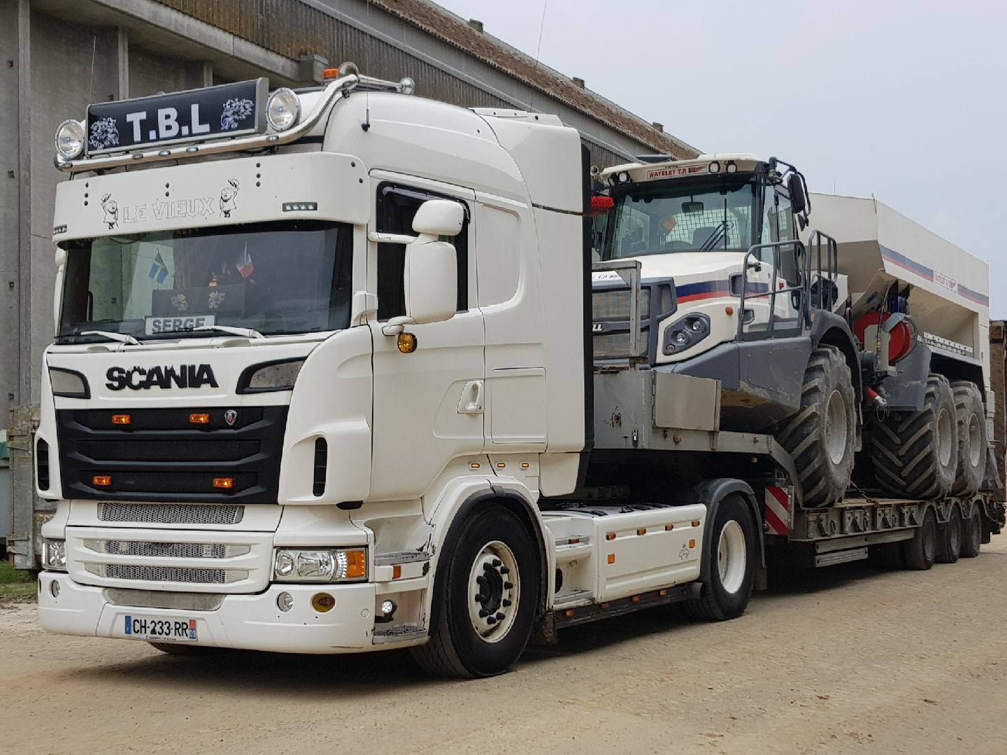 Poids lourd blanc transportant un grand engin de chantier blanc et gris