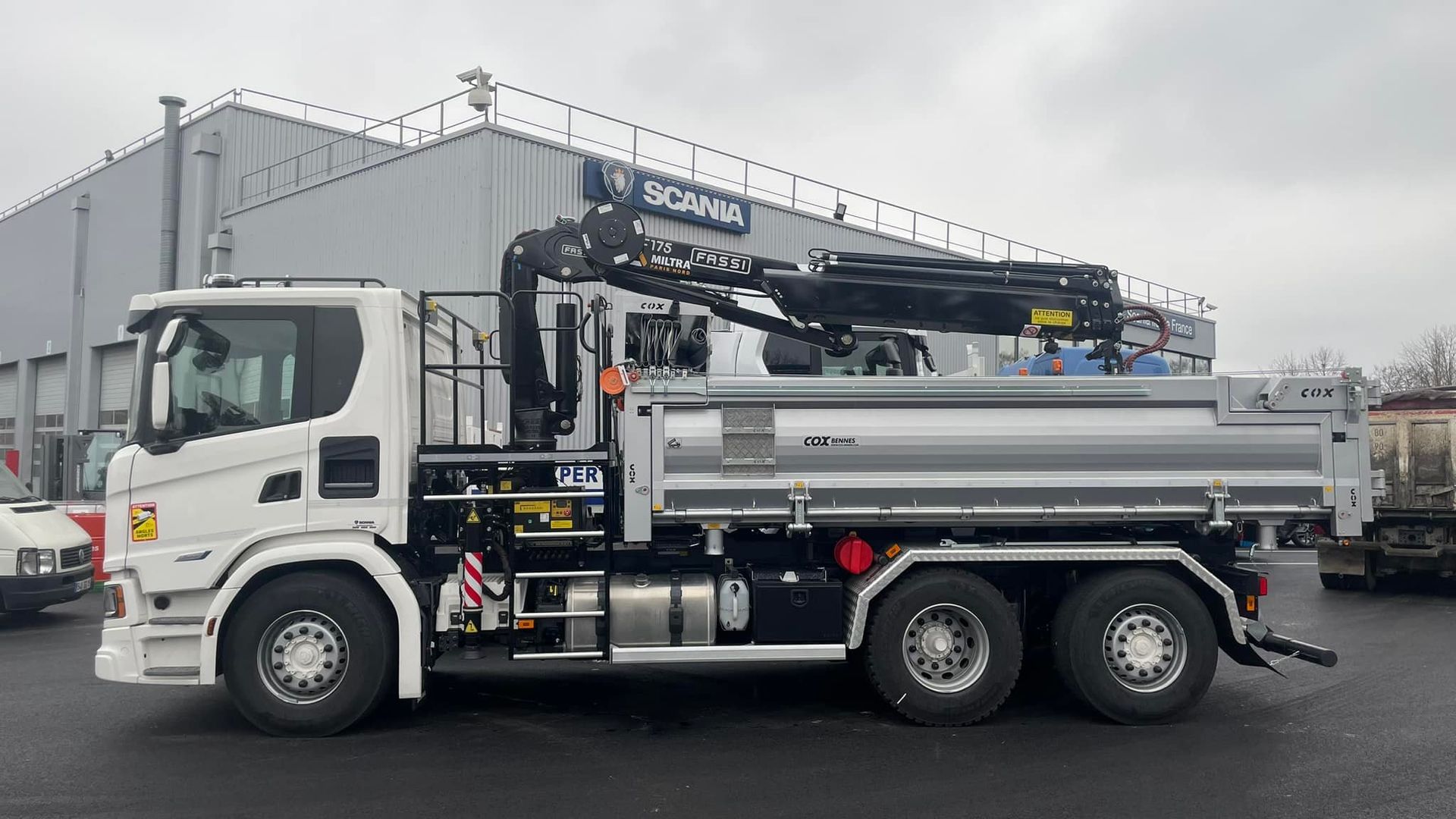 Profil d'un camion avec benne et grue devant l'enseigne Scania