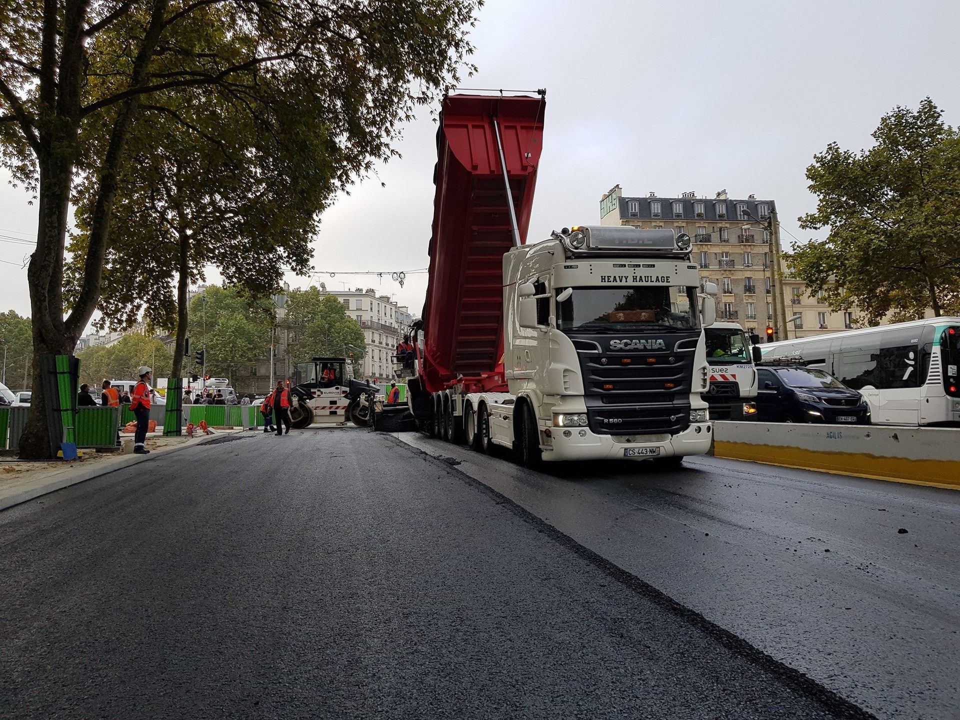Camion-benne blanc et rouge déversant son chargement d'enrobage