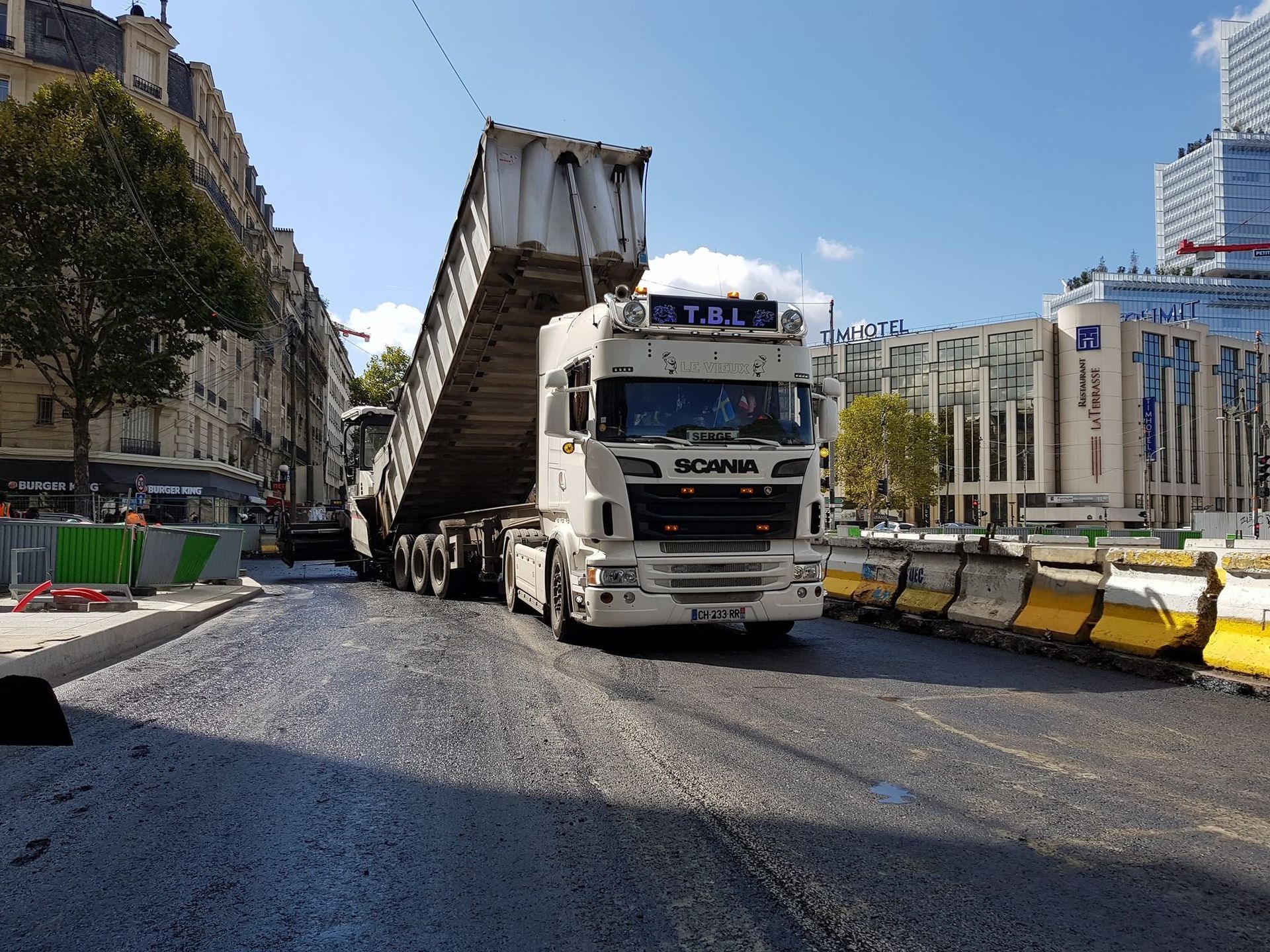 Camion-benne déversant son chargement d'enrobage sur une route en plein ville
