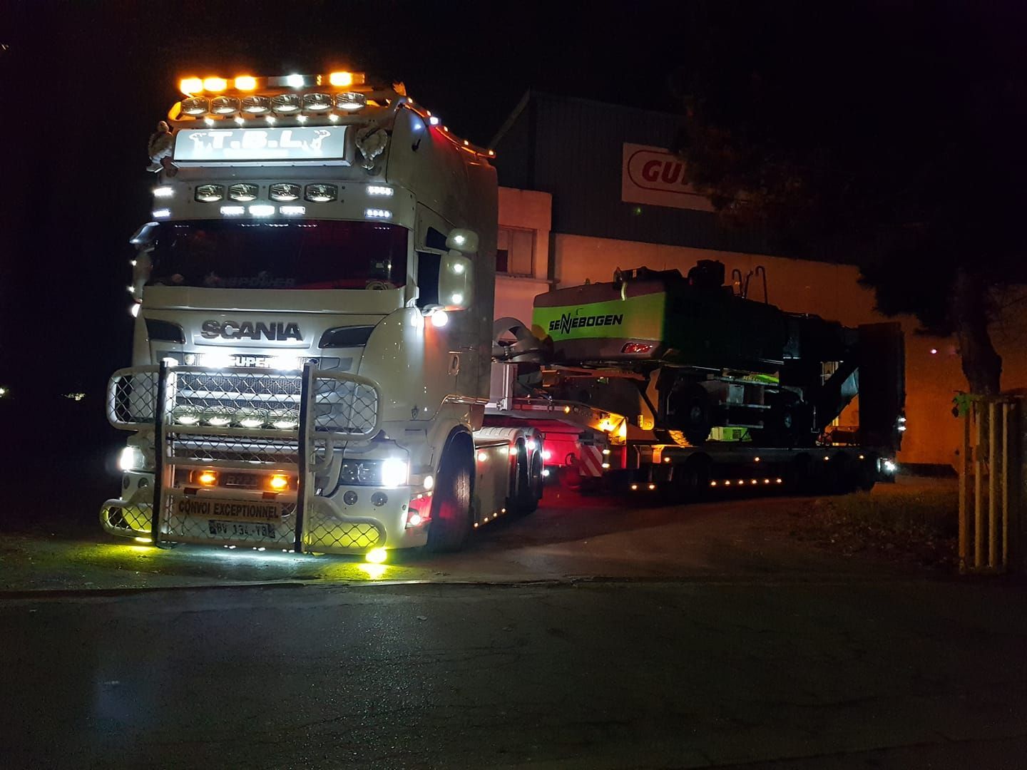 Camion blanc transportant un véhicule de chantier de nuit de couleur vert