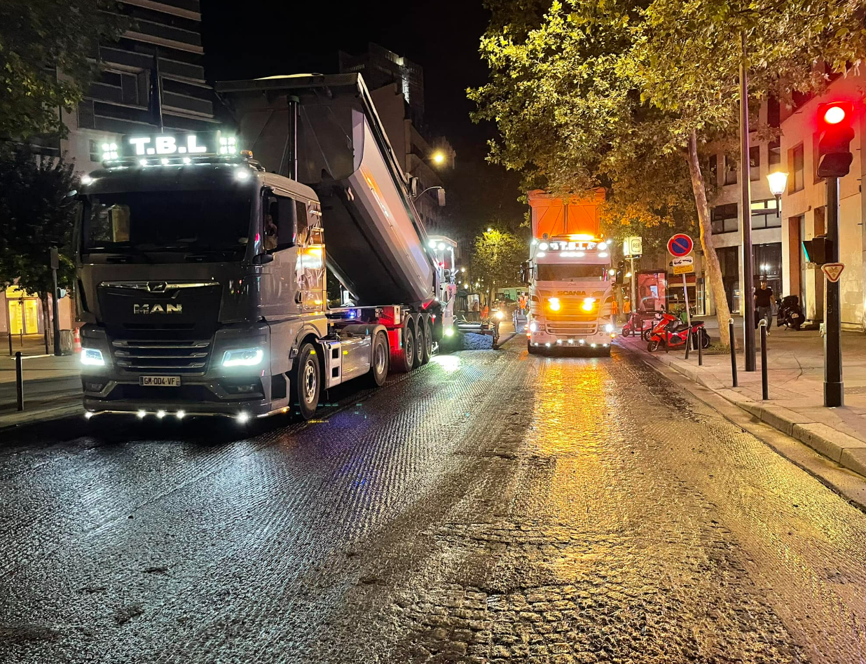 Un camion-benne de nuit en train de déverser le contenu transporté sur une route en travaux
