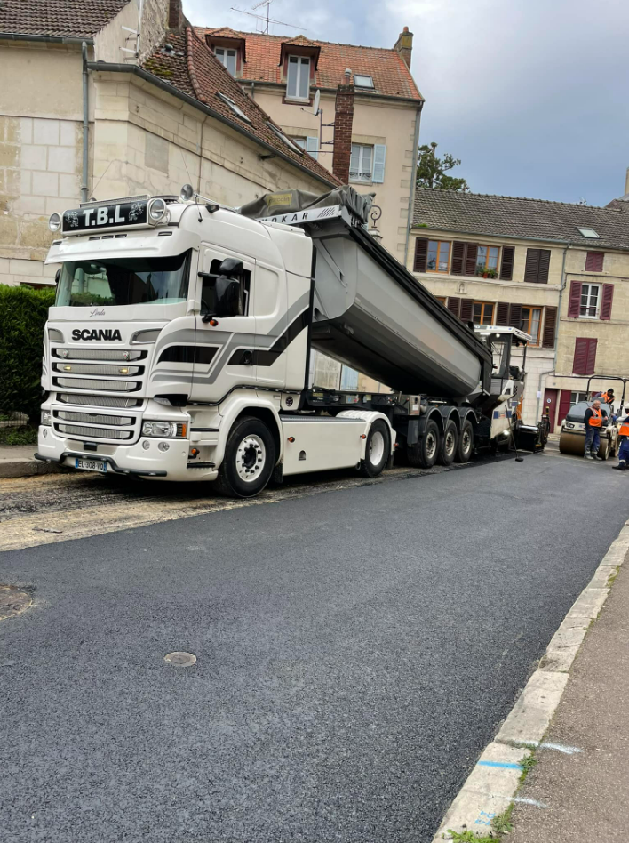 Camion-benne à côté d'une route dont l'enrobage vient d'être placé