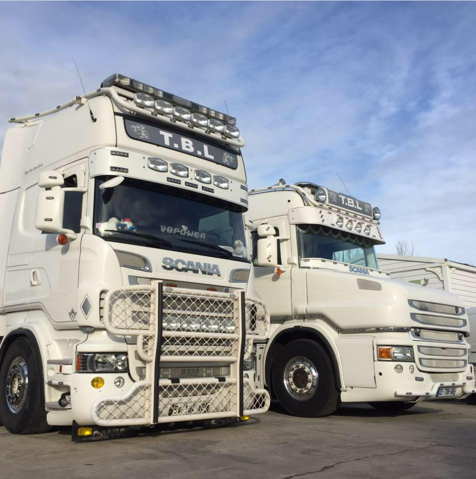 Deux grands camions blancs qui portent les initiales de TBL