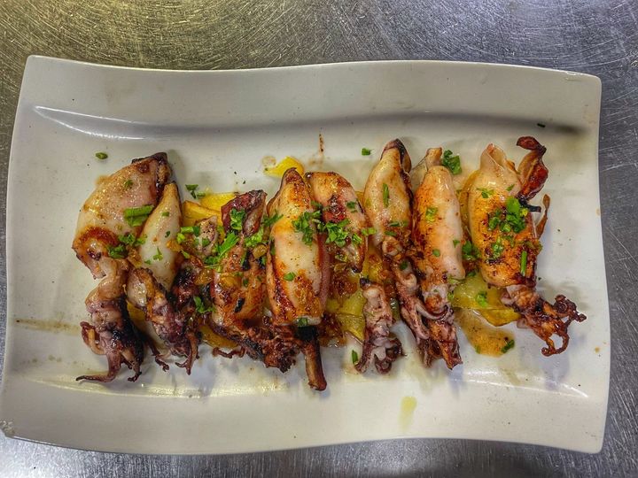 Alitas de pollo a la parrilla con hierbas y salsa, servidas en un plato rectangular blanco.